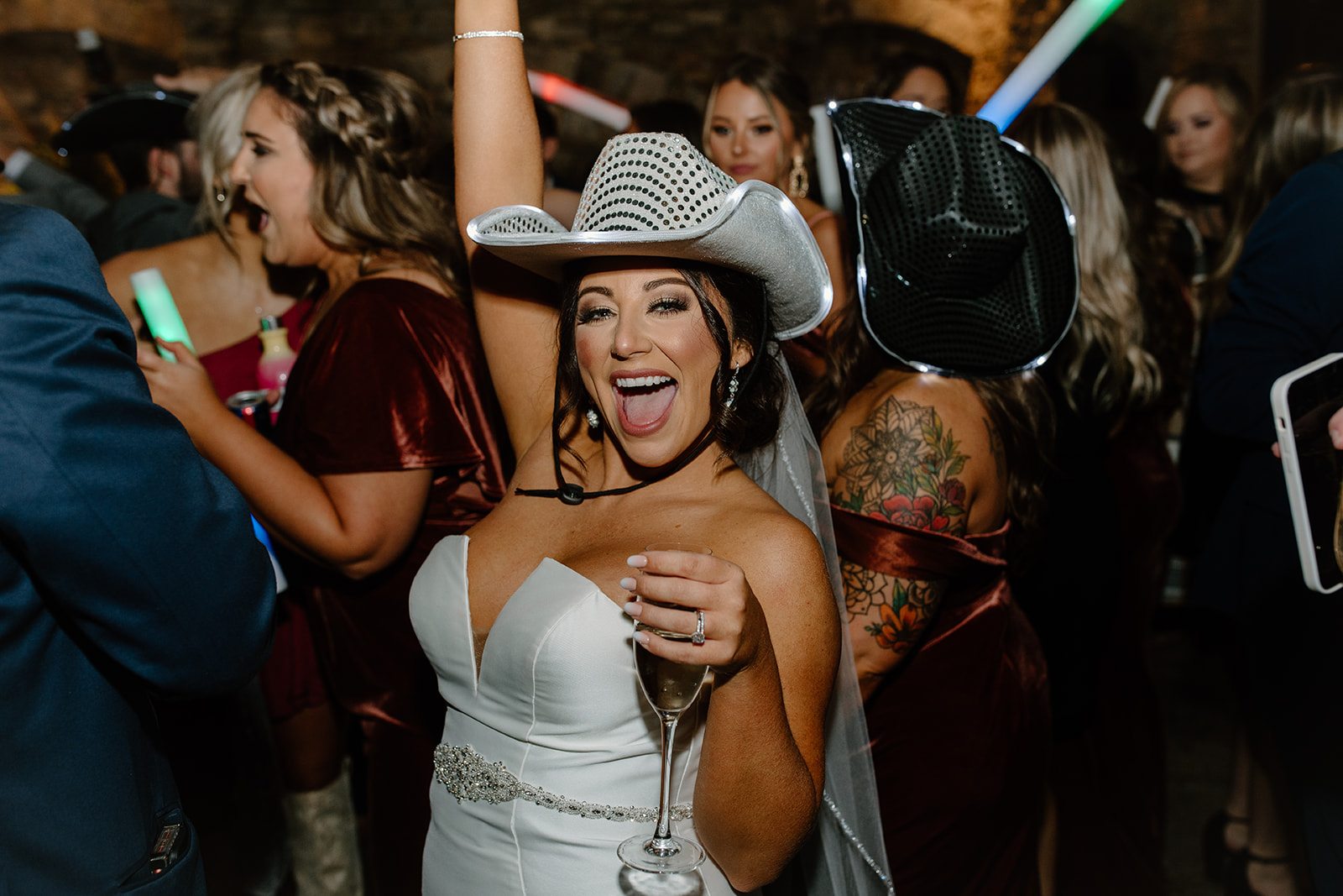 A bride in a sequined cowboy hat celebrating with her friends and glow sticks on the dance floor at a north Georgia wedding